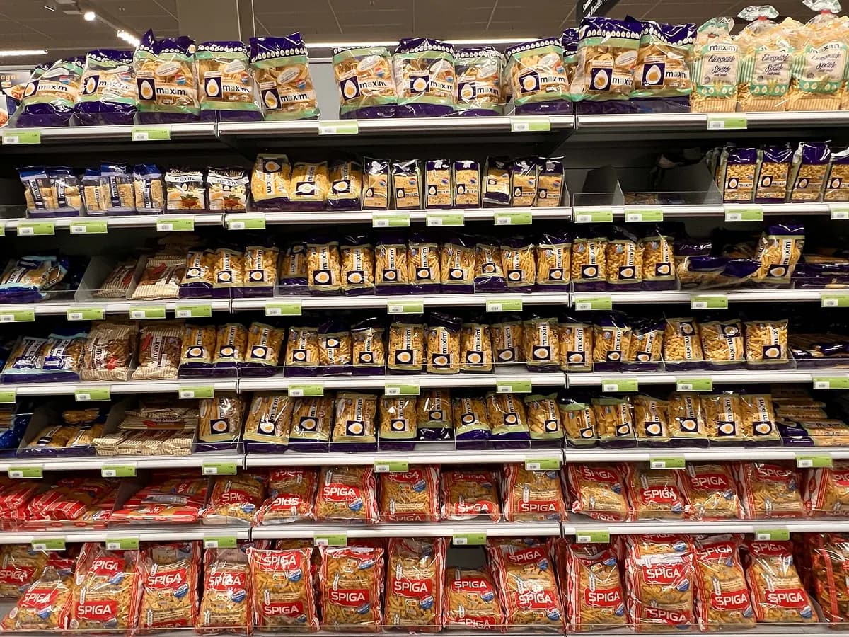 Supermarket shelf of pasta packs with product, price tag and empty-slot boxes