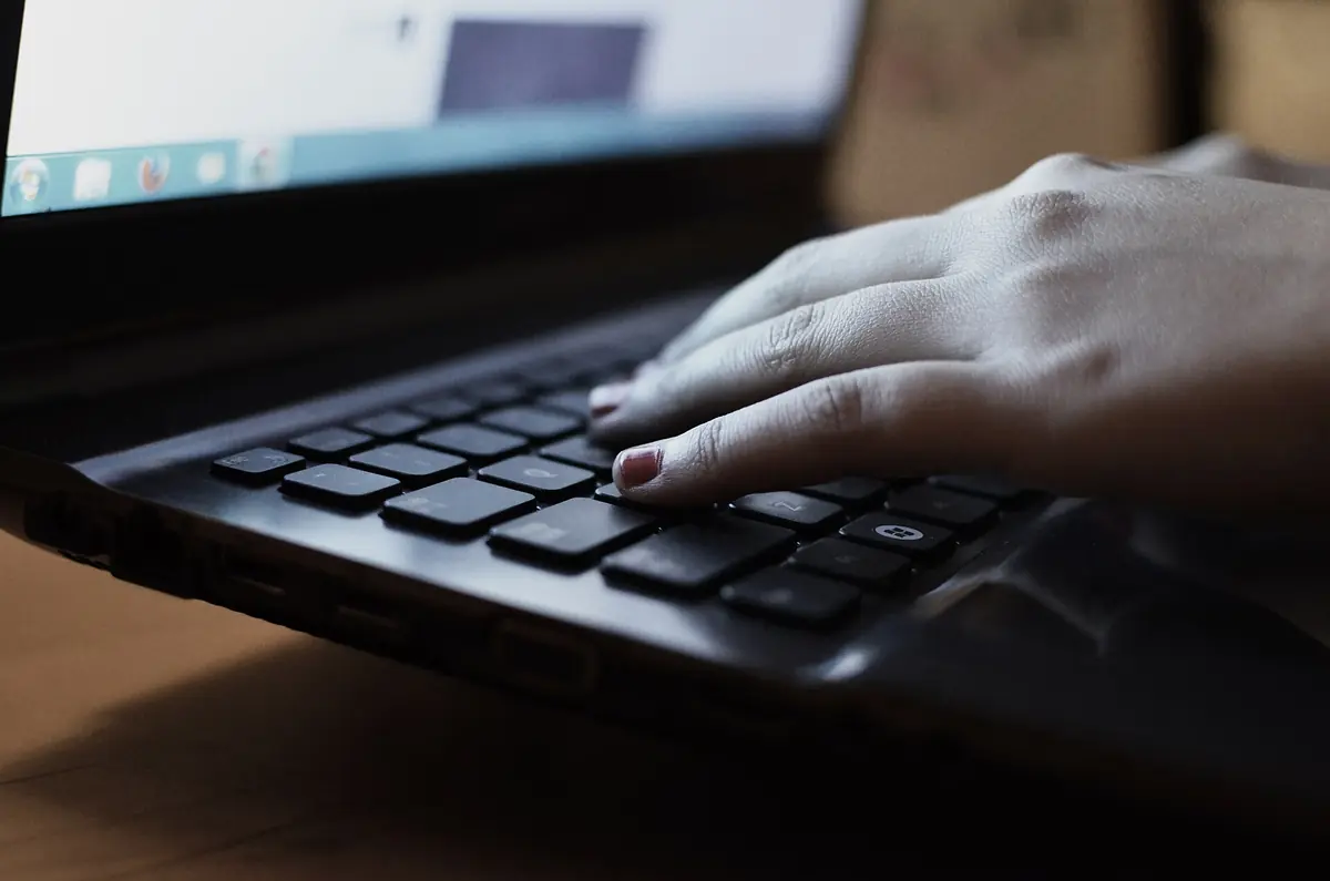 Hand on a laptop keyboard with a Bengali prompt, model answer and rubric scores overlaid